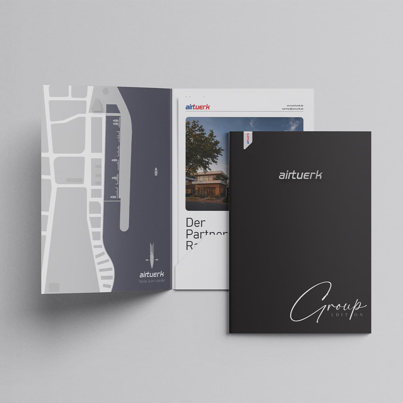 A folder set for the airtuerk Group Edition: an opened cover showing a stylised map of the Frankfurt Westhafen harbour, an inserted sheet with the airtuerk wordmark and a photograph of the headquarters, and a black outer cover carrying the wordmark and Group Edition in a script hand